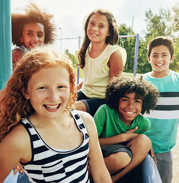 Diverse group of smiling children at a playground on a sunny day, enjoying outdoor activities together.