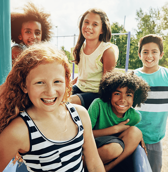 Diverse group of smiling children at a playground on a sunny day, enjoying outdoor activities together.