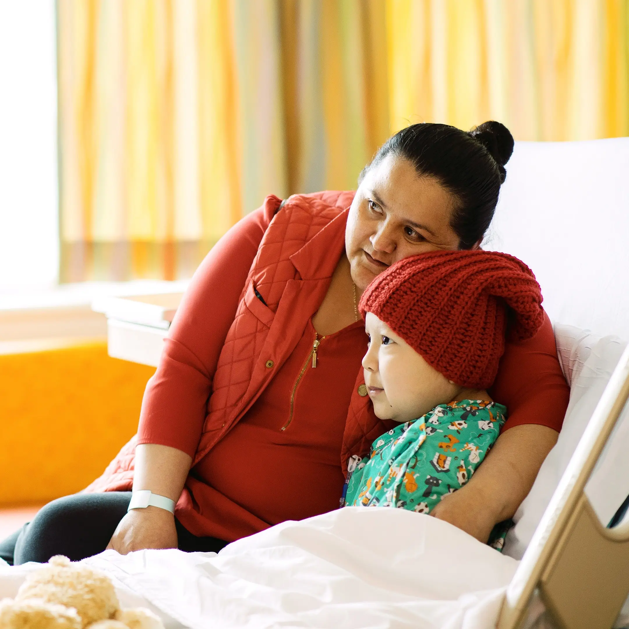 Mother snuggling son in hospital bed.