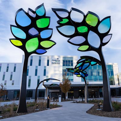 The sidewalk leading to the entrance of the new Behavioral Health & Wellness Center at Children's Nebraska, decorated with colorful stained glass sculptures of trees.