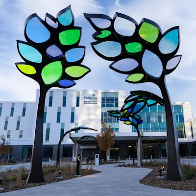 The sidewalk leading to the entrance of the new Behavioral Health & Wellness Center at Children's Nebraska, decorated with colorful stained glass sculptures of trees.