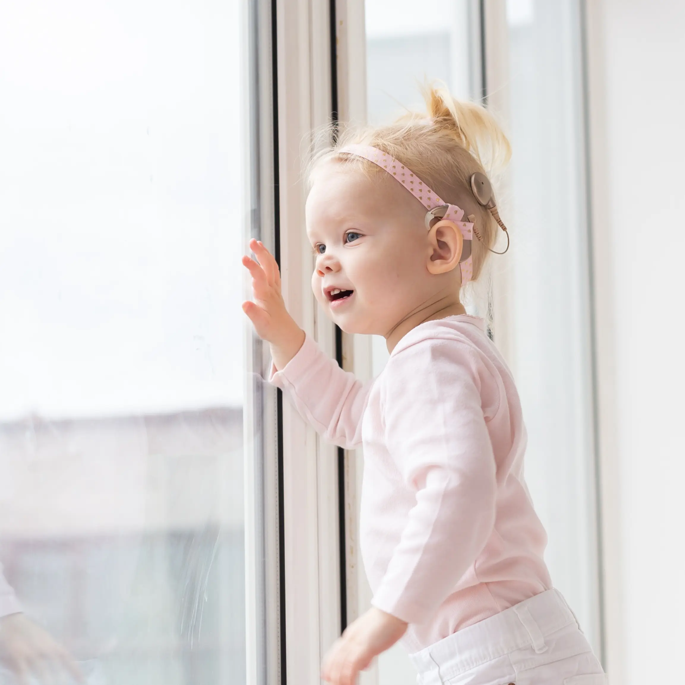 Young girl with cochlear implant looking out window.