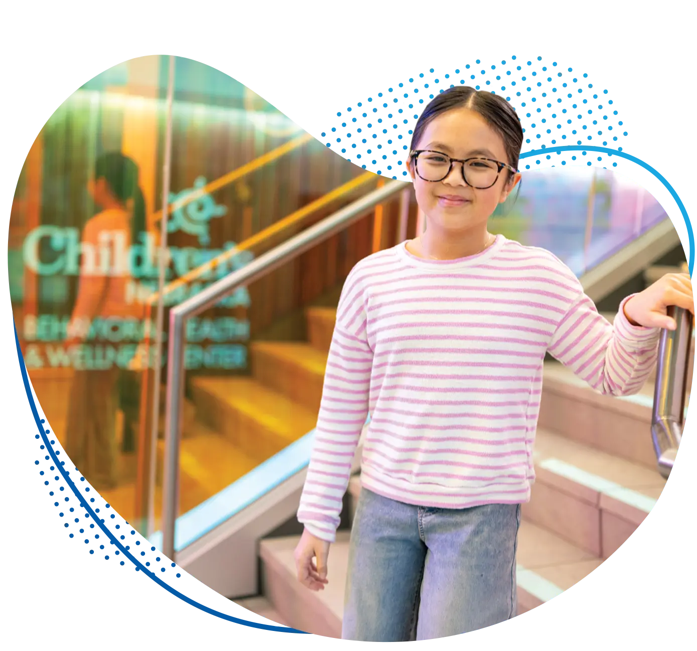 Young girl in pink striped sweater and glasses standing in the entrance of the new Behavioral Health & Wellness Center at Children's Nebraska.