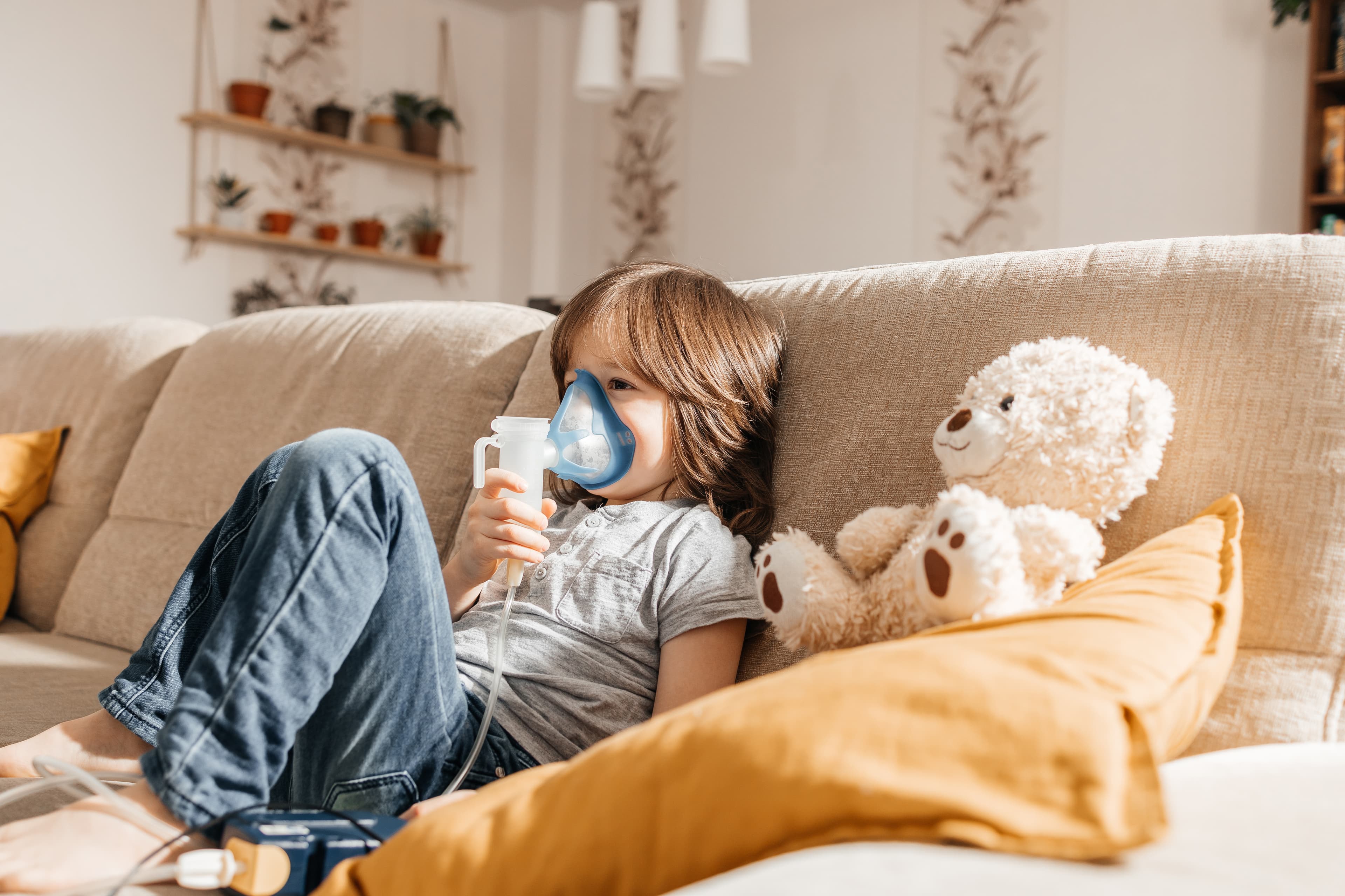 Little boy makes inhalation with a nebulizer at home lying on the couch.