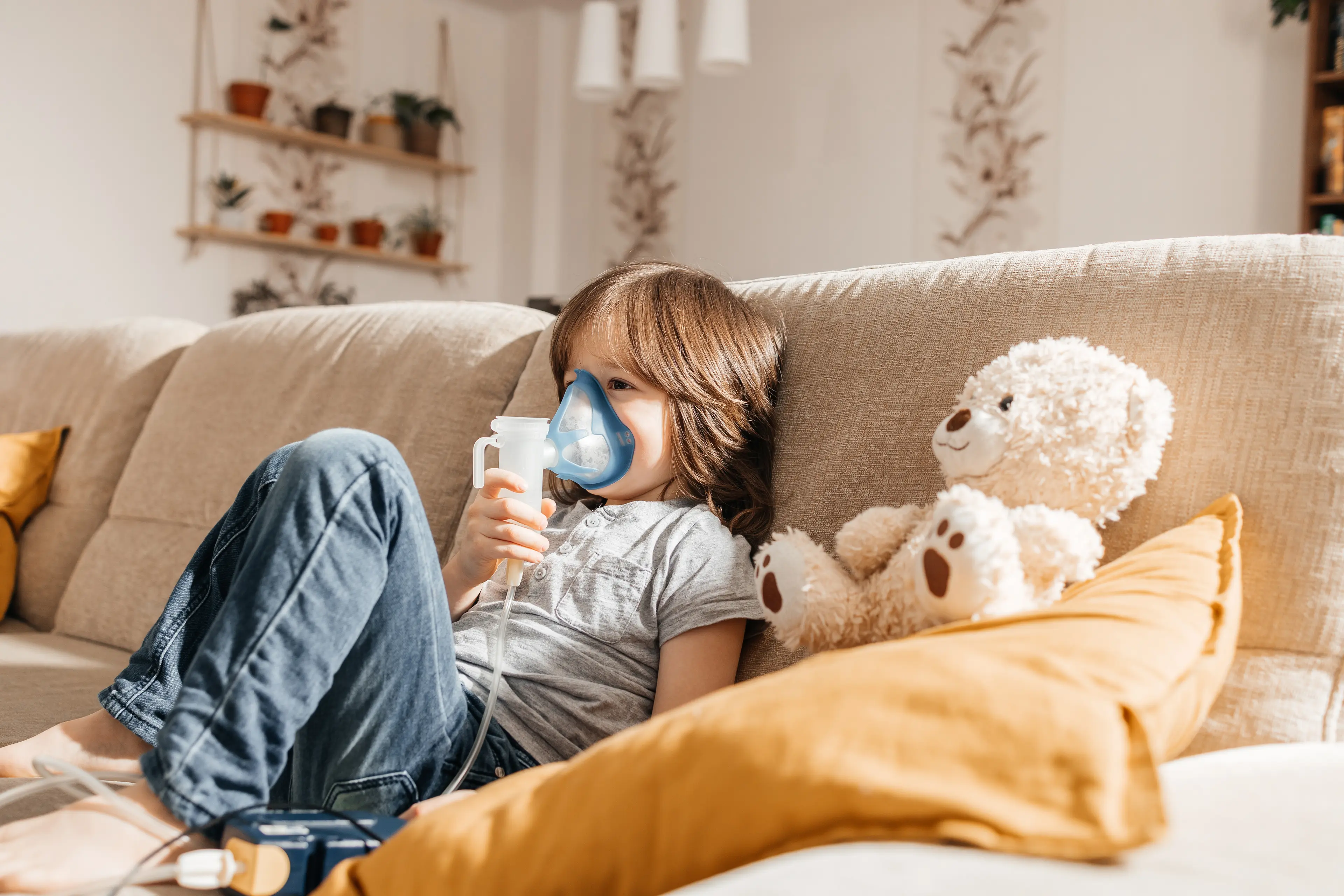 Little boy makes inhalation with a nebulizer at home lying on the couch.