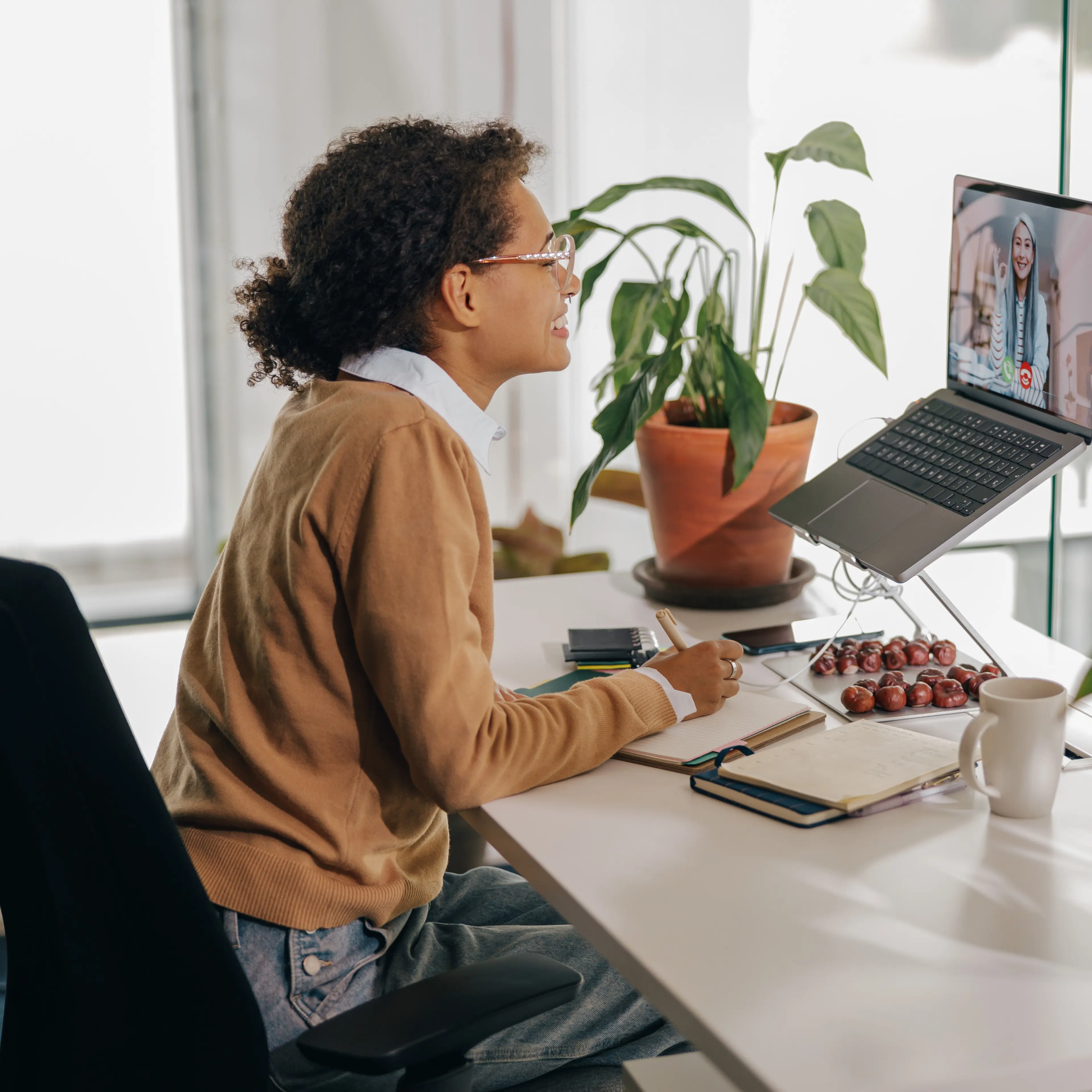 Female freelancer have video conference with client and making notes sitting in cozy coworking