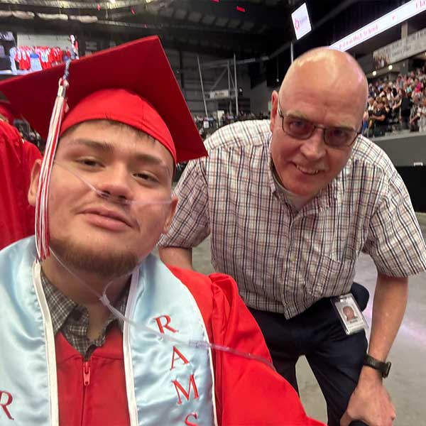 Eduardo at Graduation wearing a red cap and gown, with a family member.