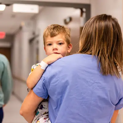 Mother carrying son down hospital hallway.