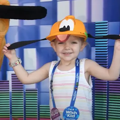 Lily, the Children's Miracle Network Champion, smiling in a picture with Pluto at Disneyland.