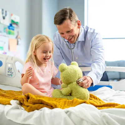 Children's Nebraska pediatric provider making young patient smile by pretending to check a stuffed animal's heart with a stethoscope.