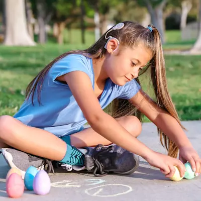 Girl with cochlear implant drawing with sidewalk chalk.