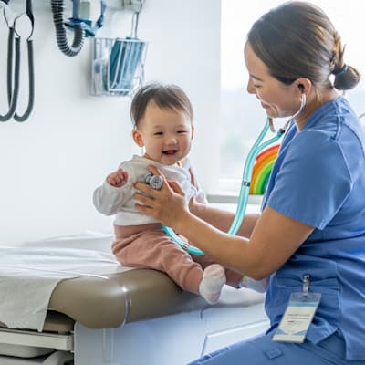 Nurse making small baby smile in exam room.