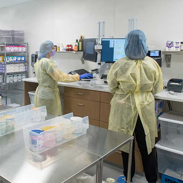 Healthcare workers in protective gowns and hairnets working at stations in the milk and formula laboratory.