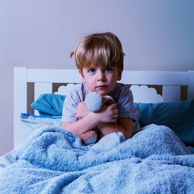Young boy sitting awake in his bed.