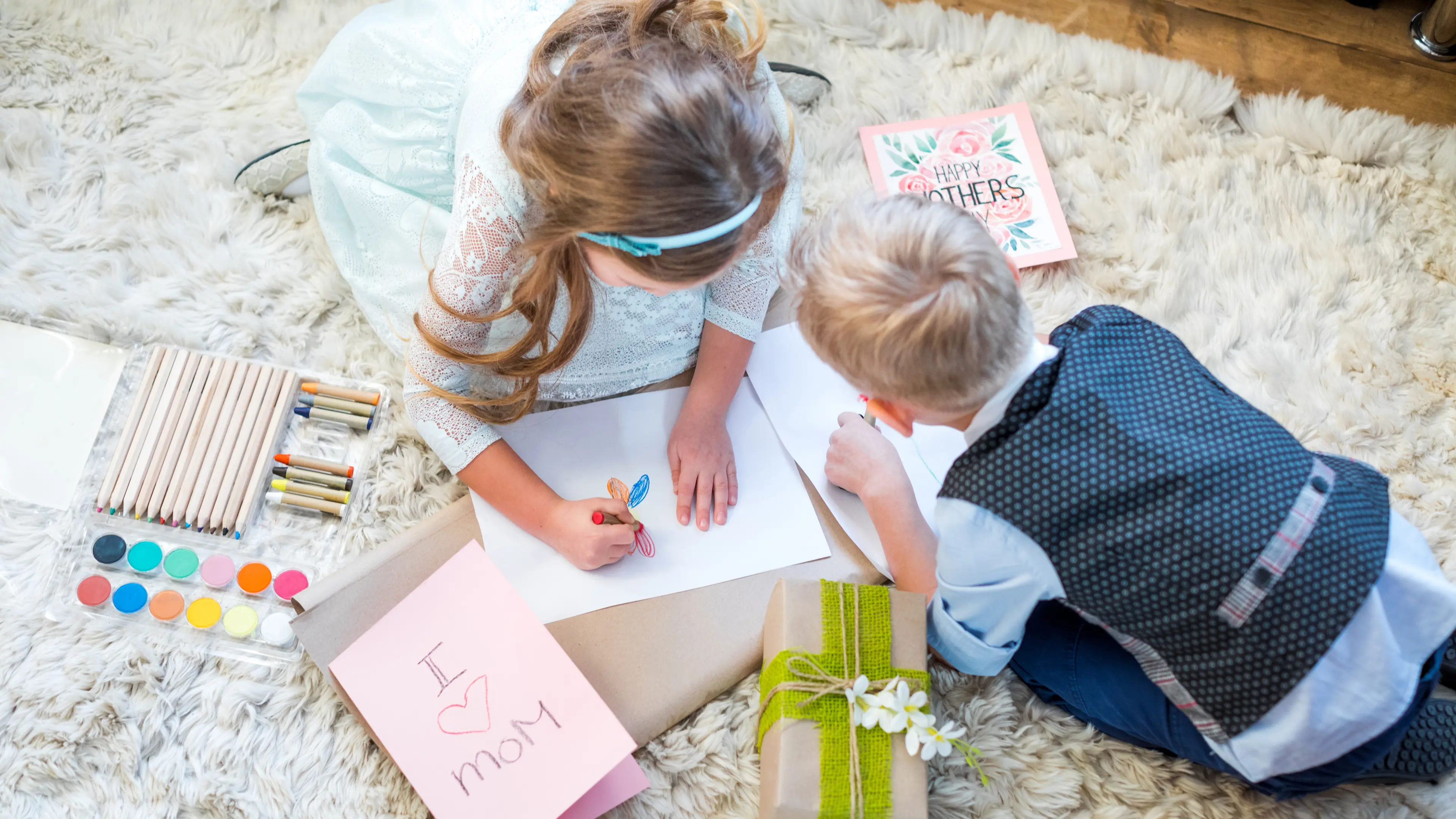 Cute little boy and girl sitting on carpet and preparing present