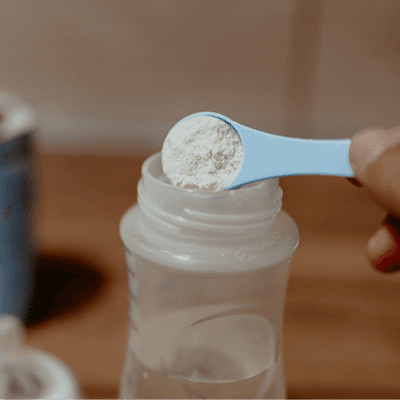Parent hand putting infant formula into baby bottle.