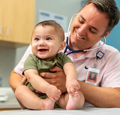 Children's Physicians primary care pediatrician playfully interacting with infant during routine exam.