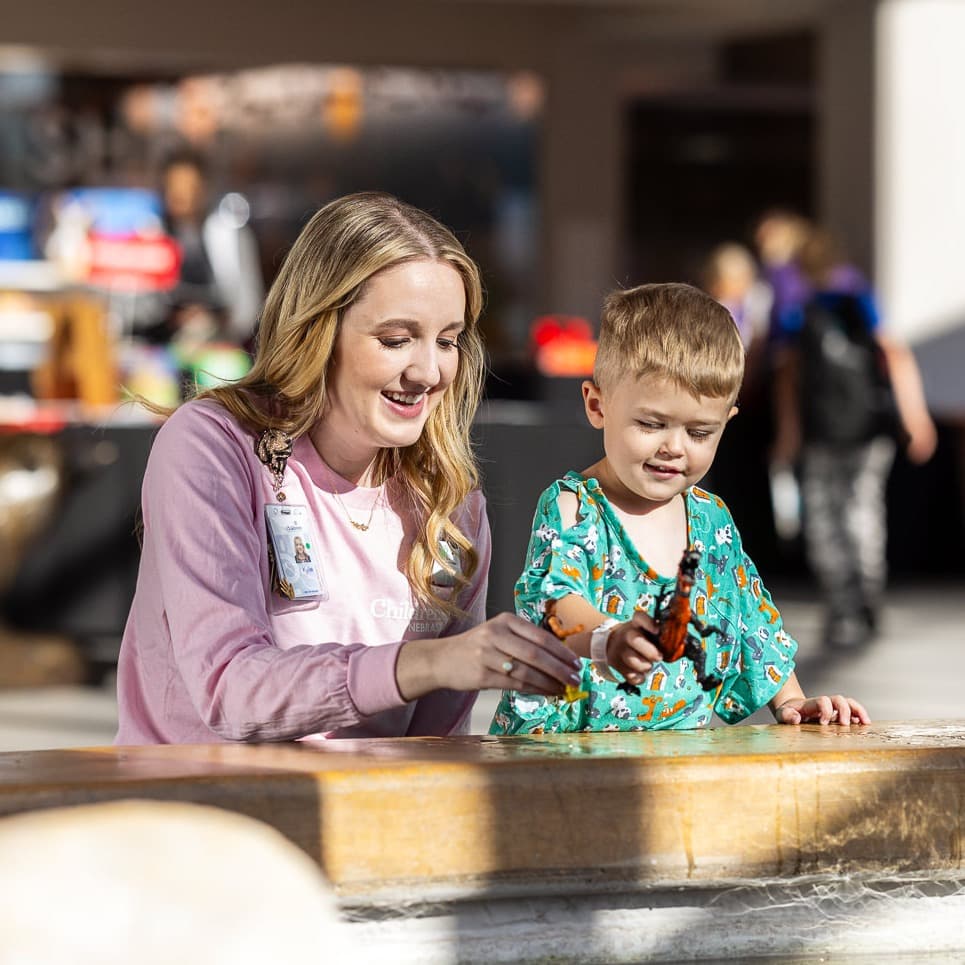 Children's Nebraska provider playing dinosaurs with a young patient in the hospital lobby.
