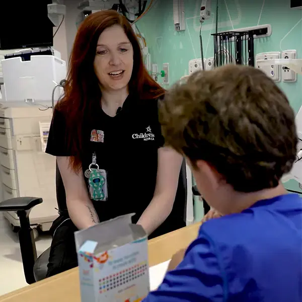 Healthcare worker in black uniform speaking with a patient in blue in a medical room with mint green walls.