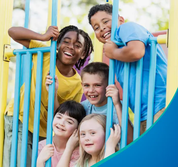 Five smiling children of diverse backgrounds playing together on a colorful blue and yellow playground structure outdoors.