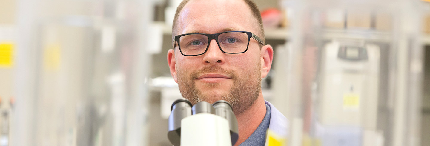 smiling researcher looks past microscope