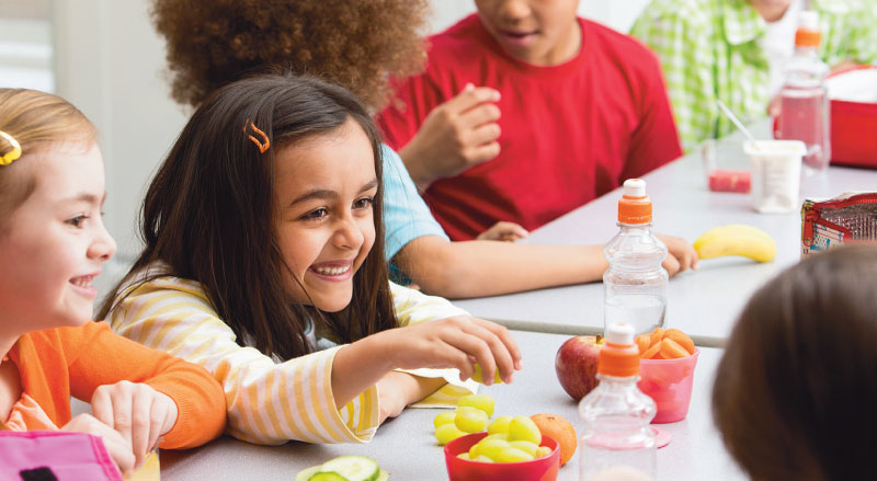 young girl smiles at lunch table with healthy food