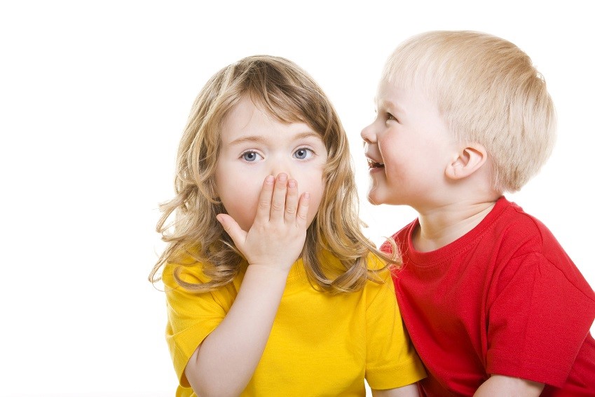 photo of a child whispering into the other's ear